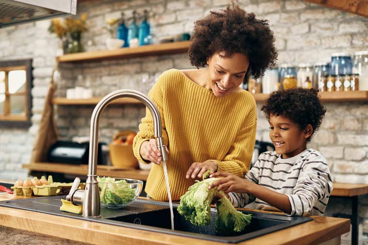 Parent and child using a sink to wash vegetables