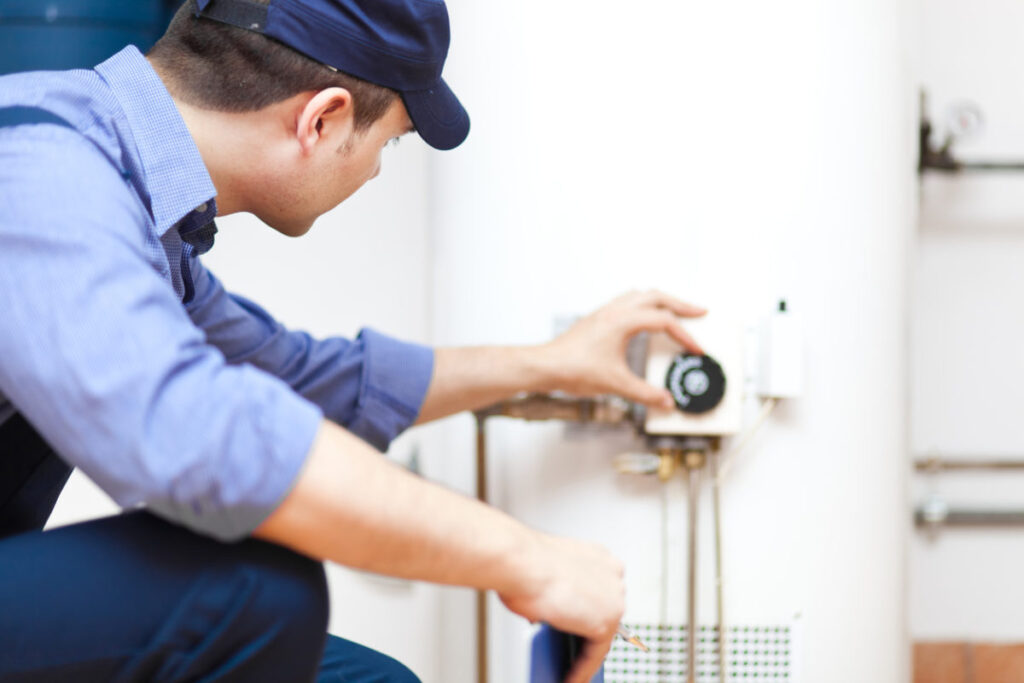 Plumber adjusting a knob on a tank-style water heater.